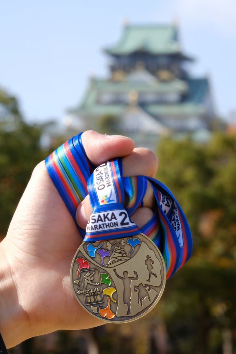 An Osaka Marathon medal held in front of Osaka Castle